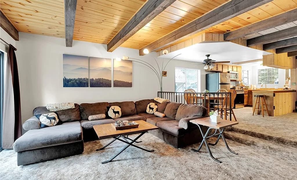 Open-concept living room with exposed beams, sectional sofa, and kitchen beyond at 2434 Fir Drive